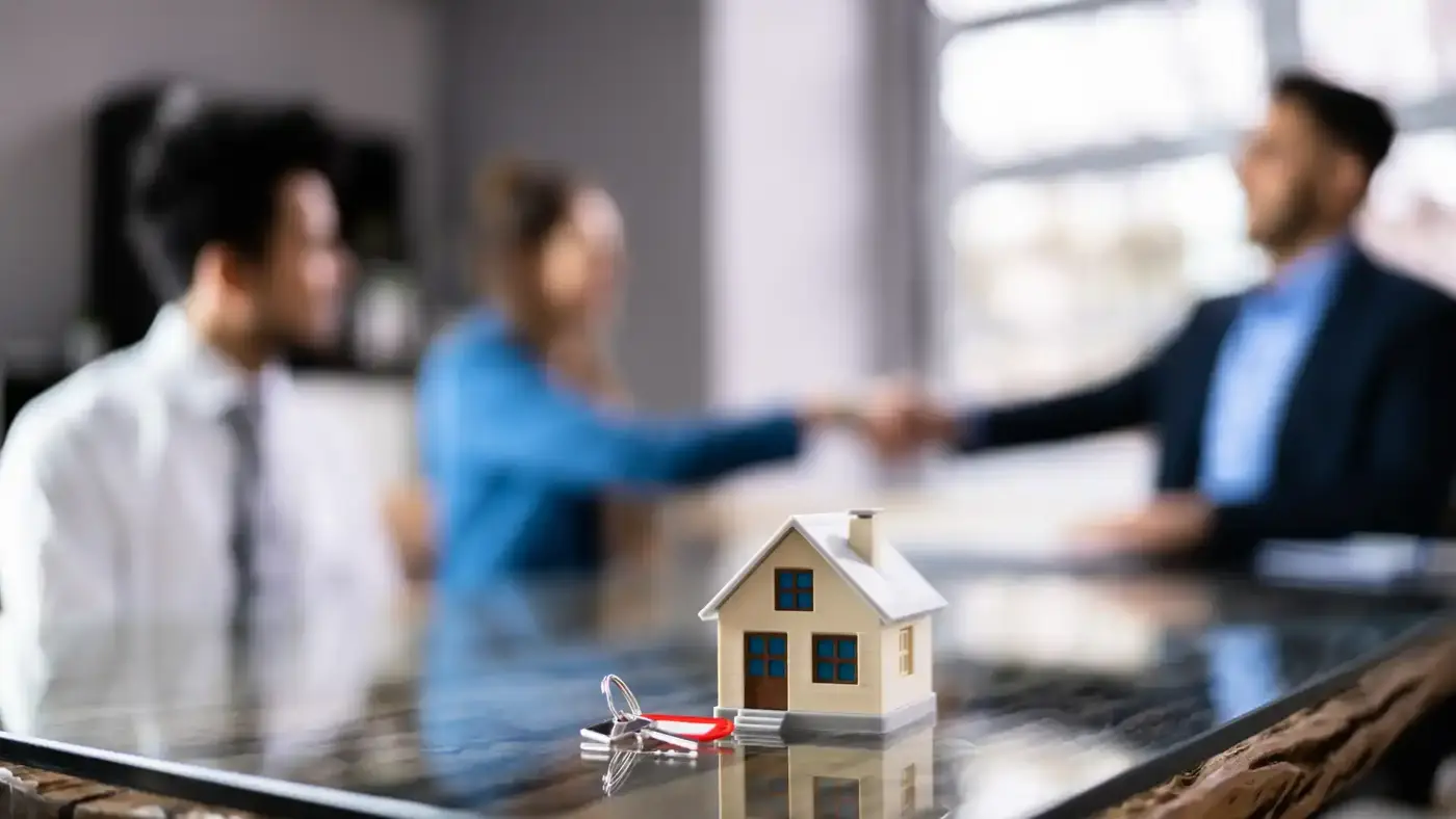 Clients shaking hands with a mortgage broker, with a model house and keys on the desk